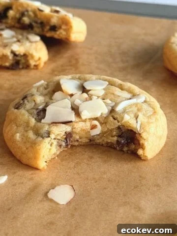 Orange almond chocolate chip cookie on parchment paper with a bite taken out of it.