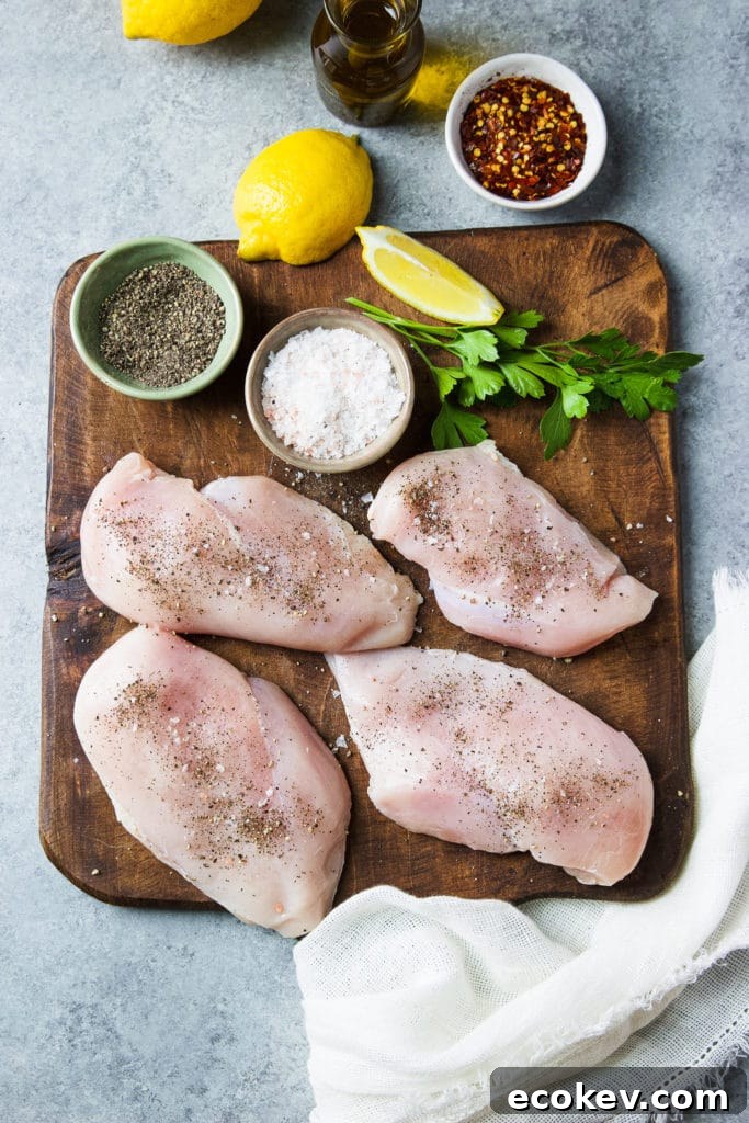 Uncooked skinless boneless chicken cutlets on a wooden chopping board surrounded by spices
