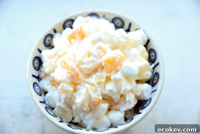 Mini marshmallows, mandarin oranges, pineapple and coconut mixed together in sour cream in a peacock-patterned bowl.