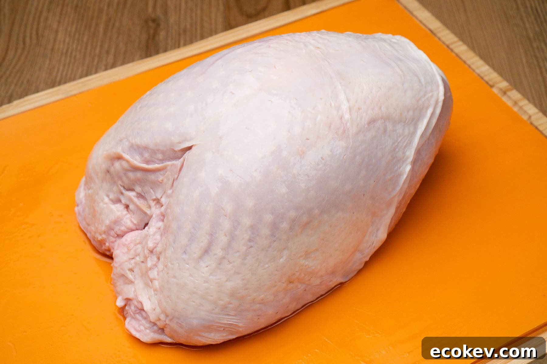 A raw turkey crown on an orange chopping board