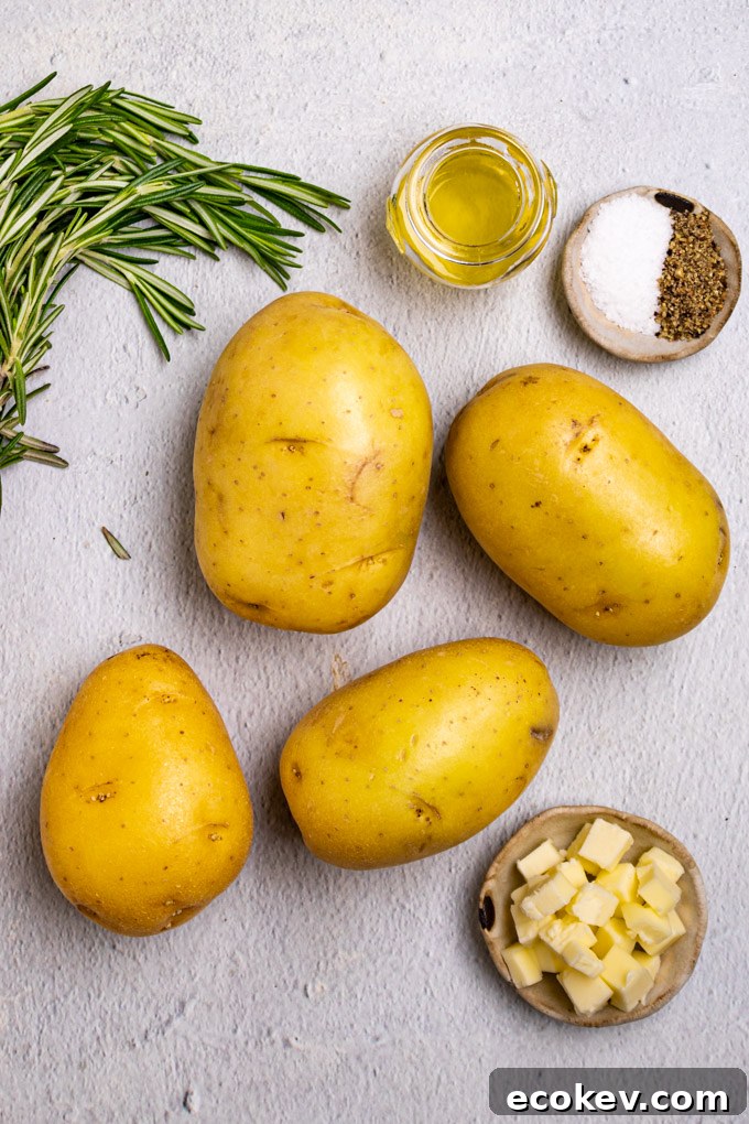 Yukon gold potatoes, rosemary springs, bowl of oil, salt and pepper, and cubes of butter are arranged on gray background.