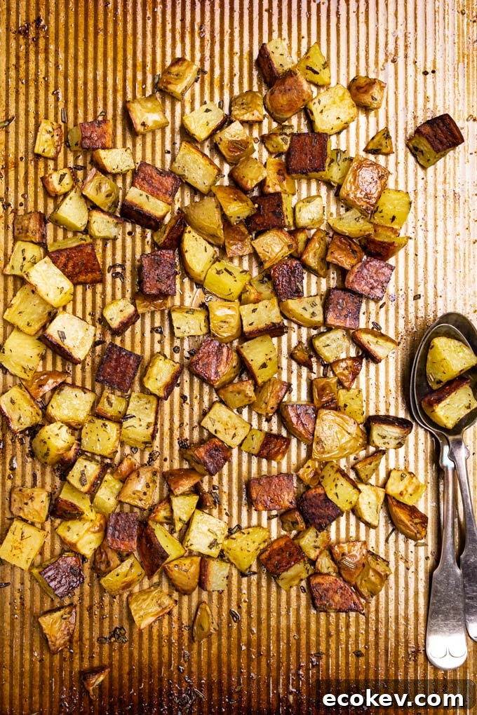 Roasted potatoes are on a baking sheet. Two spoons are laying beside the potatoes.