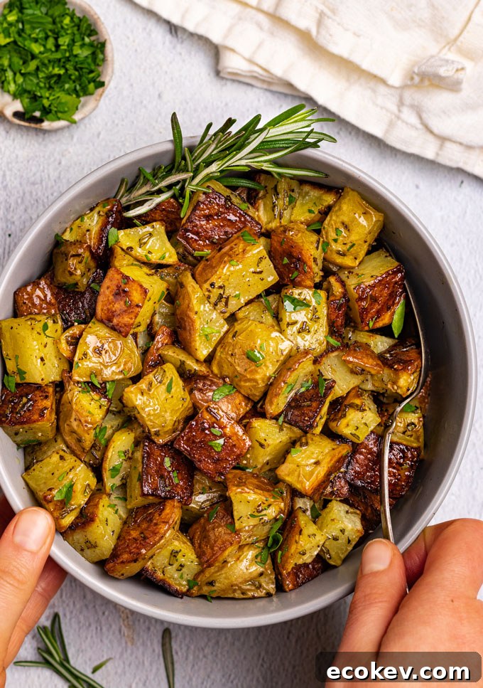 Roasted potatoes are in a gray bowl with two hands holding the bowl. Parsley is sprinkled over the potatoes.