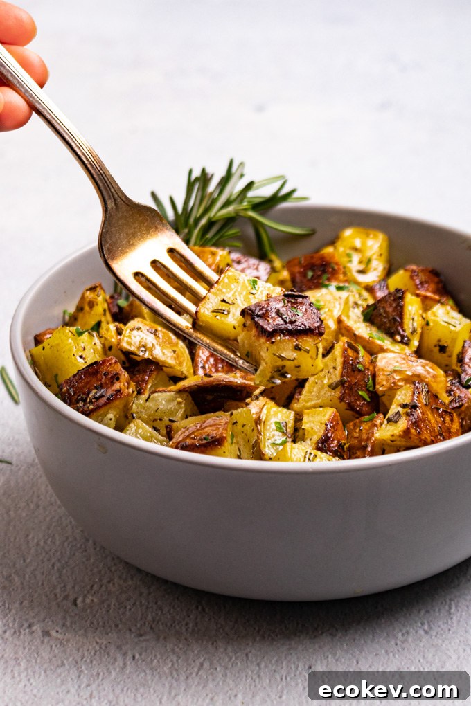 An angled shot of roasted potatoes in a bowl with a fork scooping some of the potatoes up.