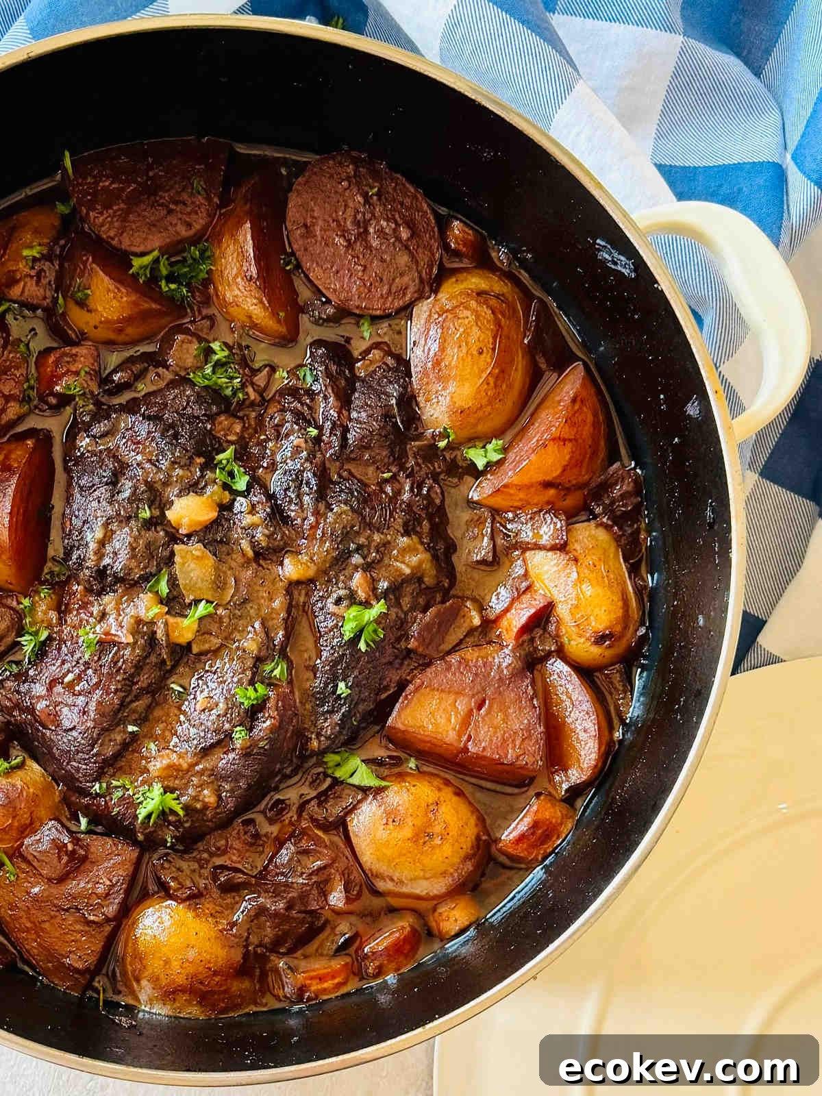 braised chuck roast surrounded by potatoes and vegetables in a dutch oven.