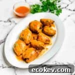 Air fryer buffalo chicken thighs on a white serving platter with extra hot sauce for dipping beside it.