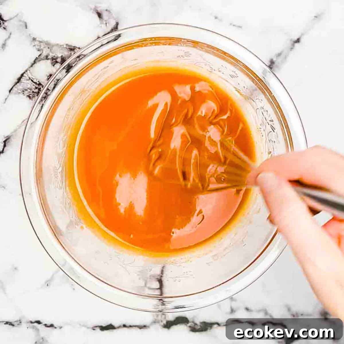 A hand using a whisk to mix the ingredients for the buffalo sauce in a small bowl.