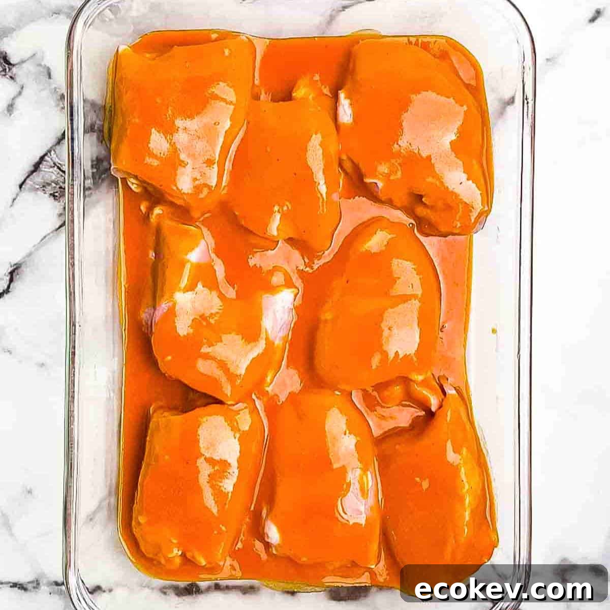 The chicken thighs in a baking dish marinating in buffalo sauce.