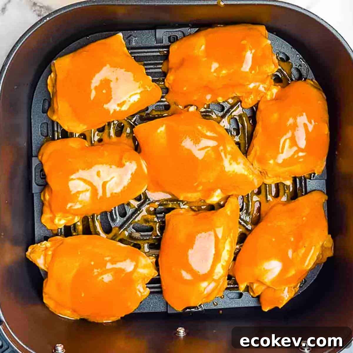 The marinated buffalo chicken thighs in the air fryer basket in a single layer.