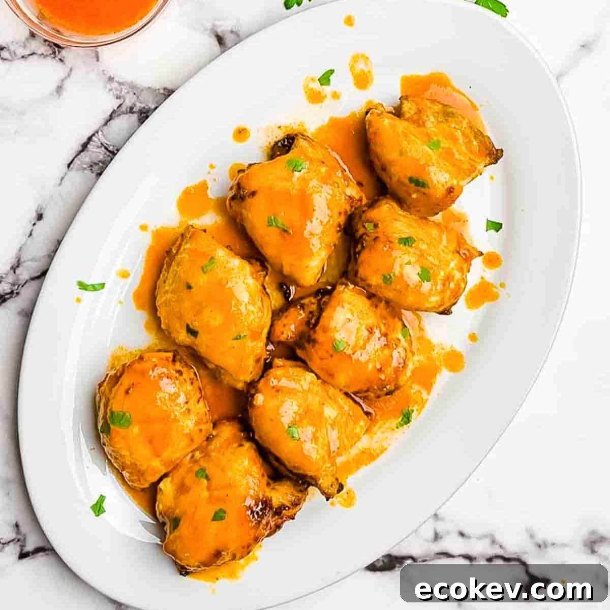 The air fried buffalo chicken thighs on a white serving platter, garnished with fresh herbs.