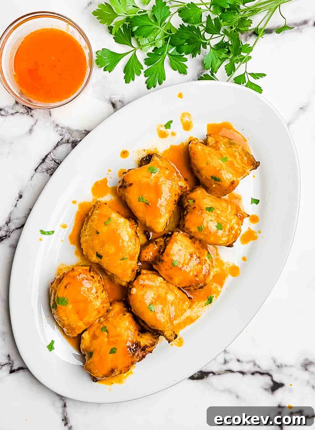 Juicy buffalo chicken thighs on a white serving platter, garnished with fresh herbs.