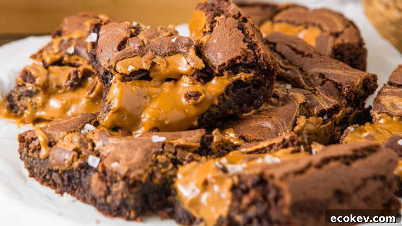 Close-up of a stack of gooey caramel-filled Biscoff Brownies, sprinkled with flaky sea salt, on parchment paper.