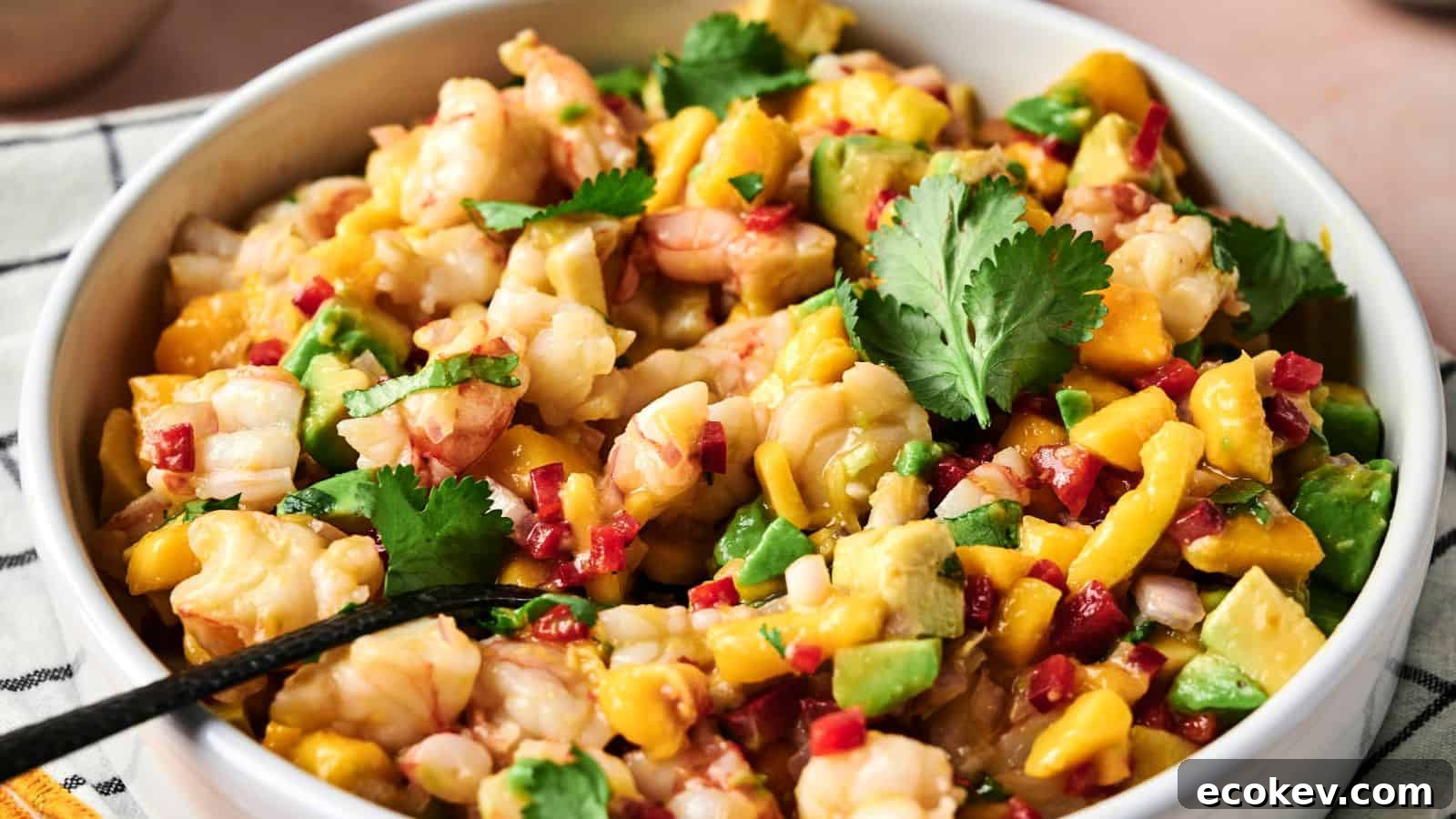 A bowl of shrimp ceviche with diced mango, avocado, red onion, red pepper, and cilantro, with a spoon inside.