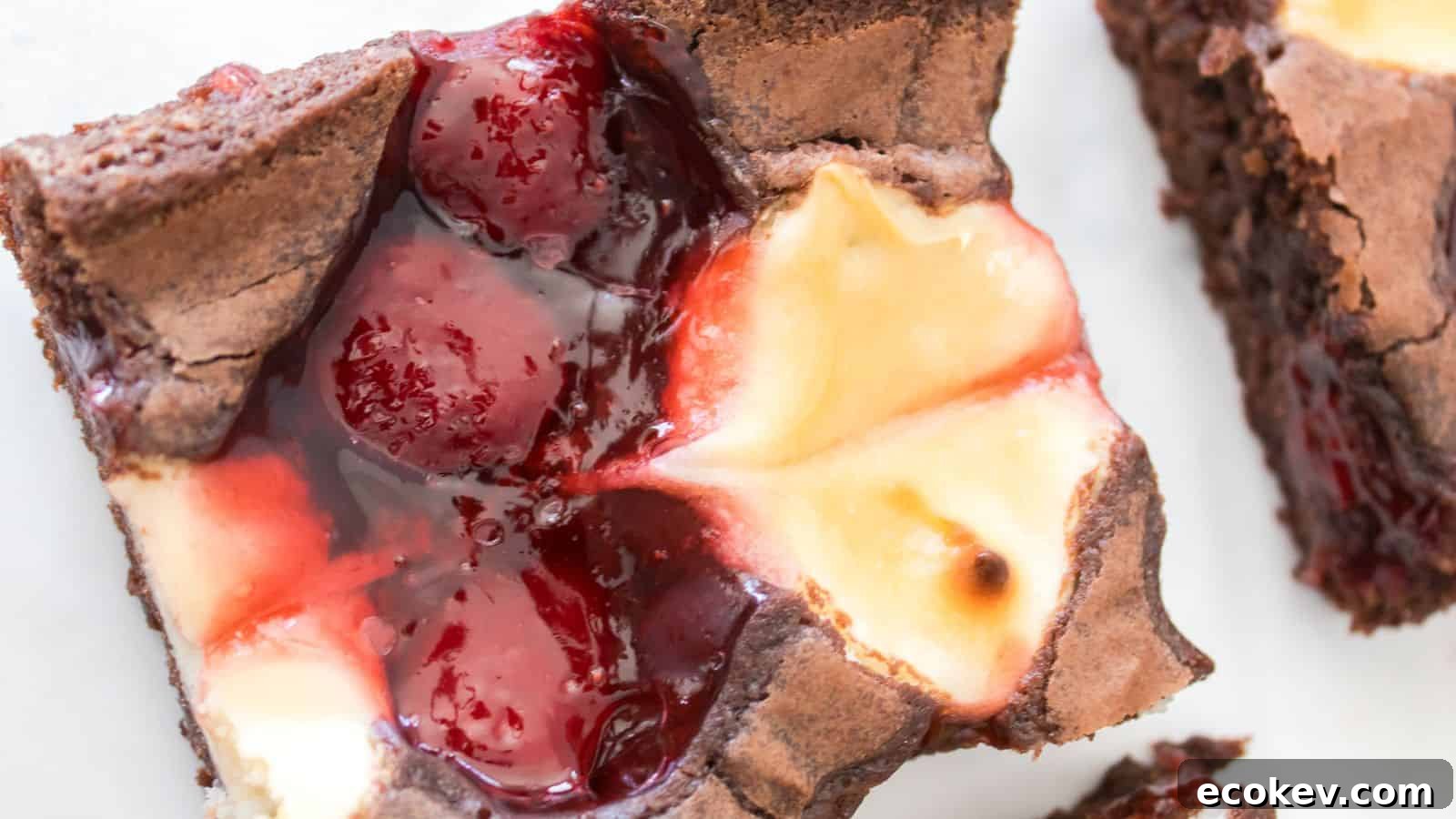 A close-up of a brownie square topped with a swirl of cheesecake and cherry filling.