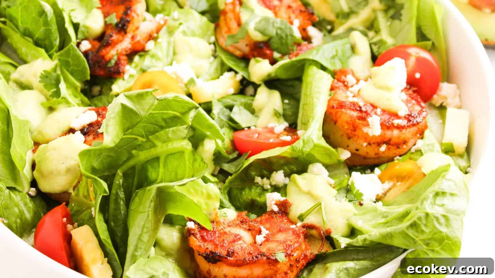 A bowl of mixed salad with grilled shrimp, avocado, cherry tomatoes, lettuce, feta cheese, and a creamy dressing.