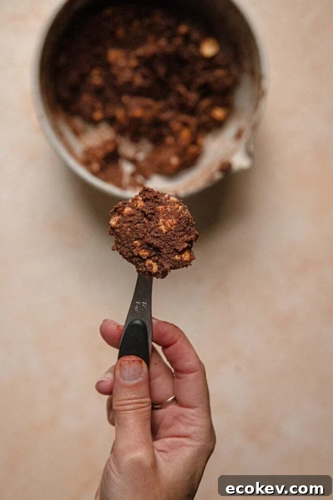 A hand holding a tablespoon with cookie dough.