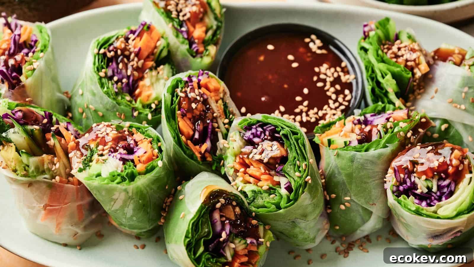 A plate of fresh vegetable spring rolls sliced in half, arranged around a dish of dipping sauce and sprinkled with sesame seeds.