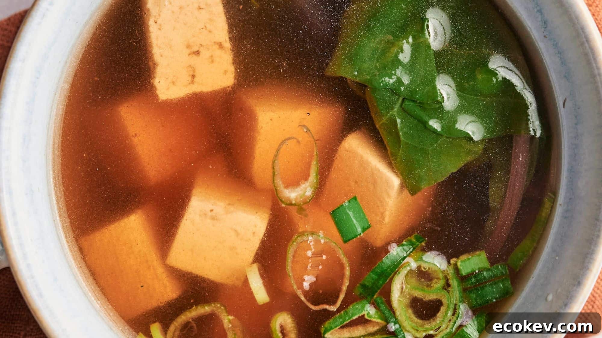 A bowl of miso soup with tofu cubes, seaweed, and green onions.