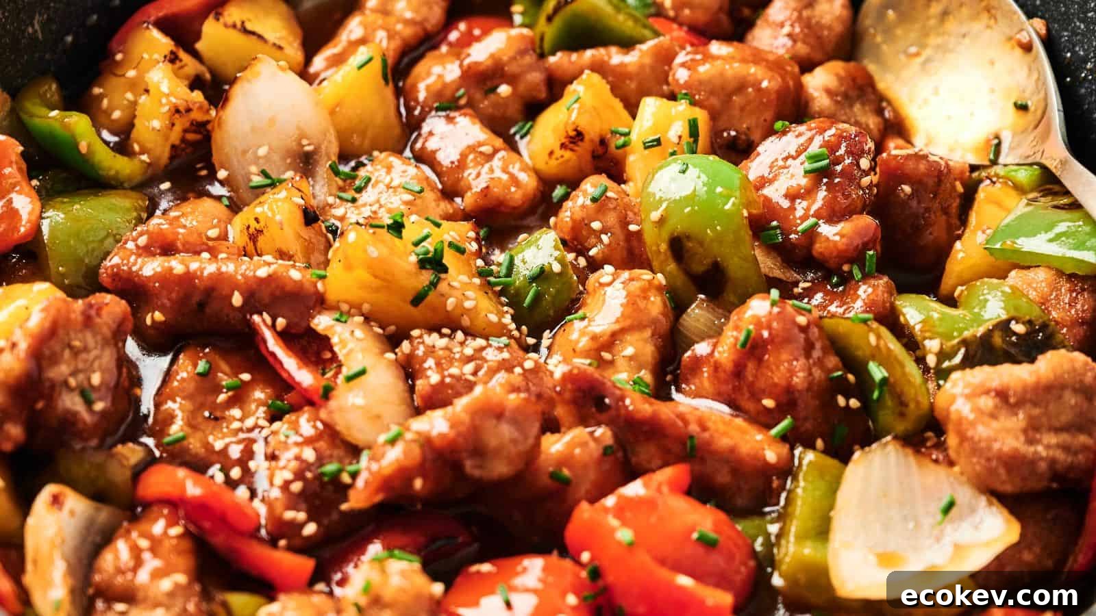 Close-up of sweet and sour pork with chunks of bell peppers, onions, and pineapple, garnished with sesame seeds and chives.