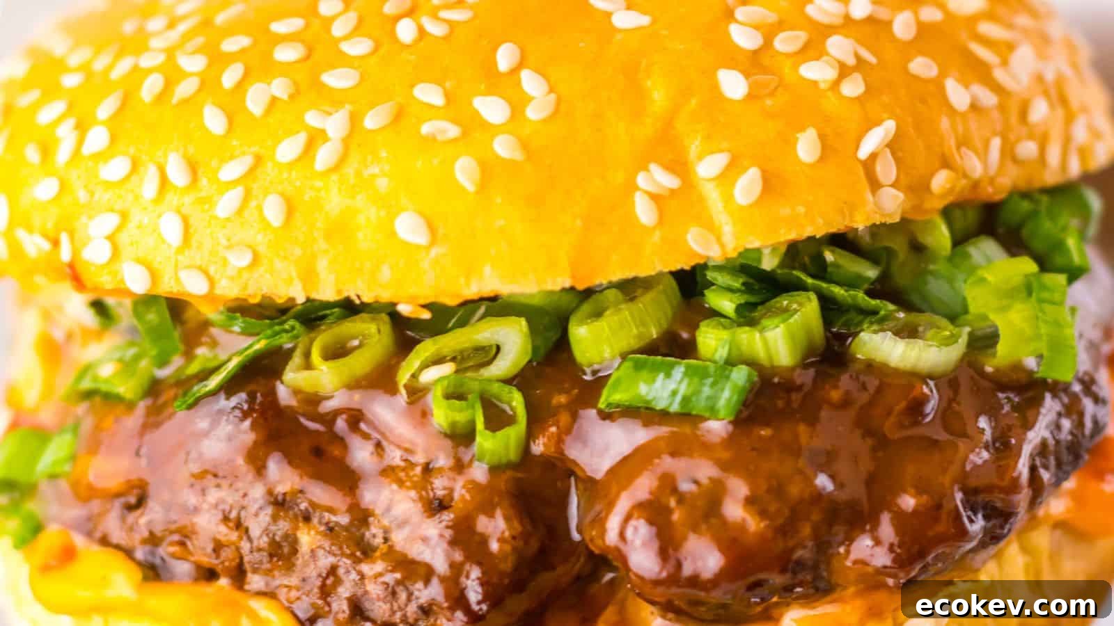 Close-up of a hamburger with a sesame seed bun, beef patty, green onions, and rich brown sauce.