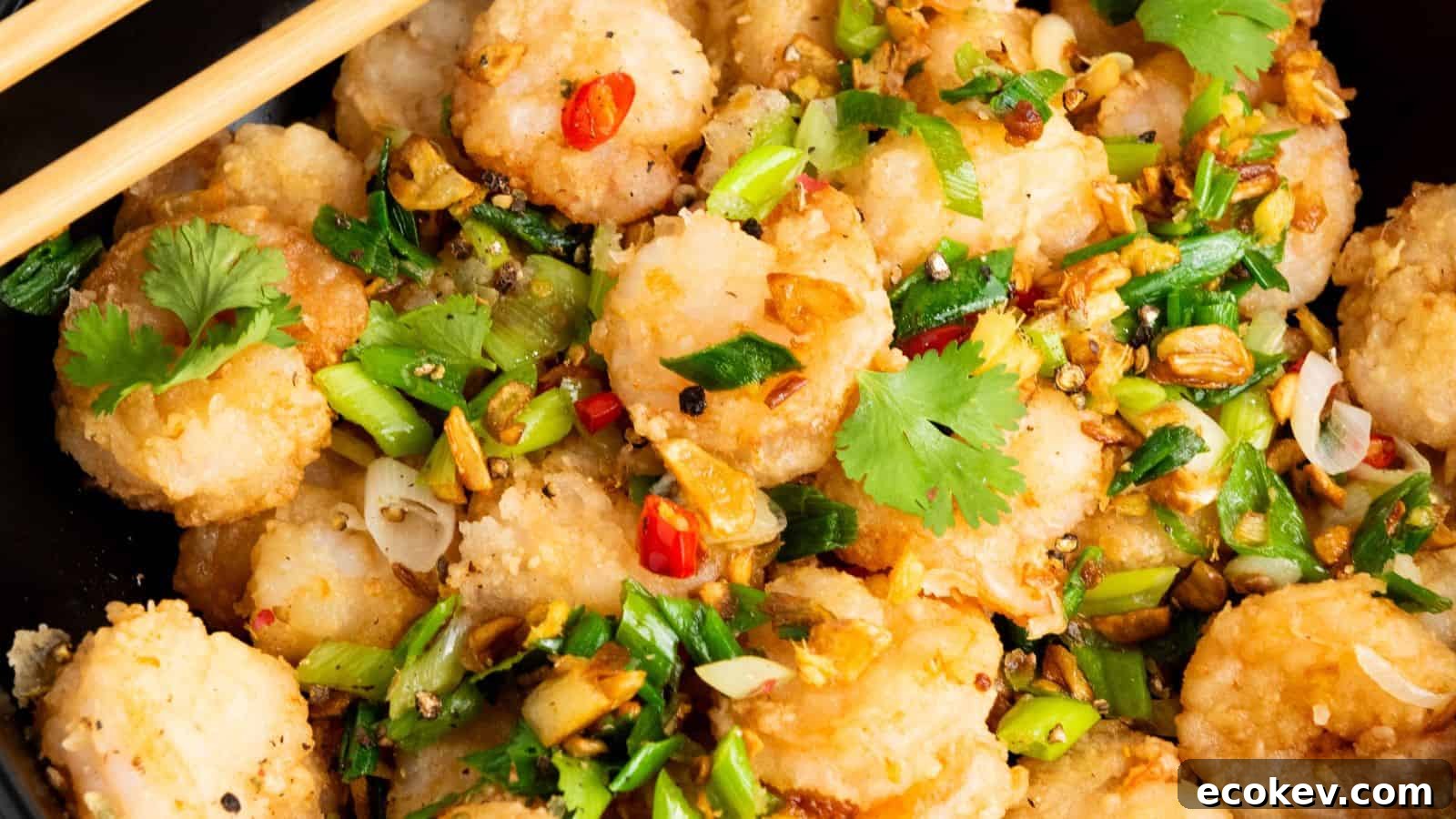 A close-up of a serving of shrimp garnished with chopped green onions, red chili slices, and cilantro, placed in a bowl with chopsticks on the side.