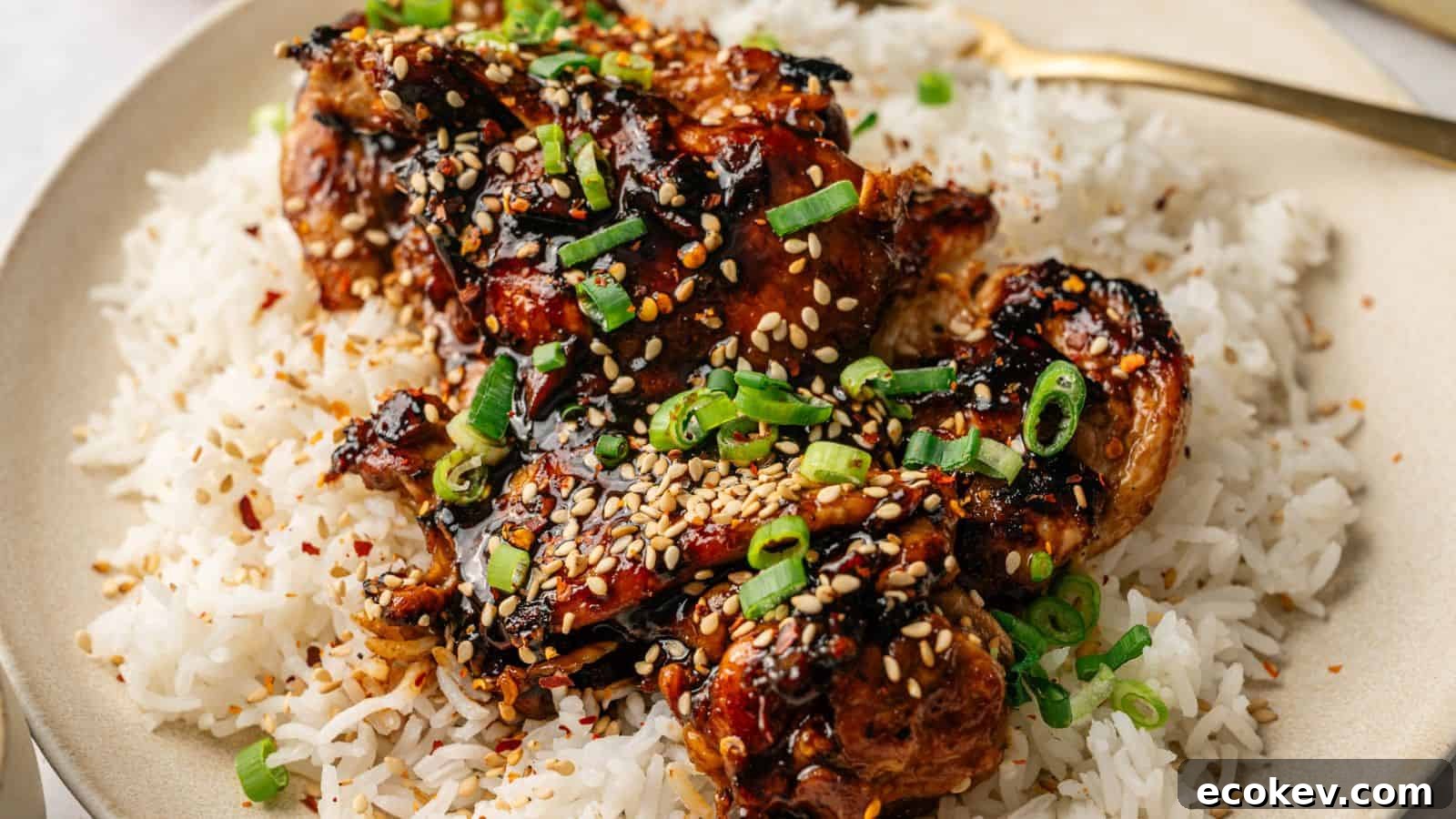 A plate of white rice topped with glazed chicken pieces, garnished with sesame seeds and chopped green onions.
