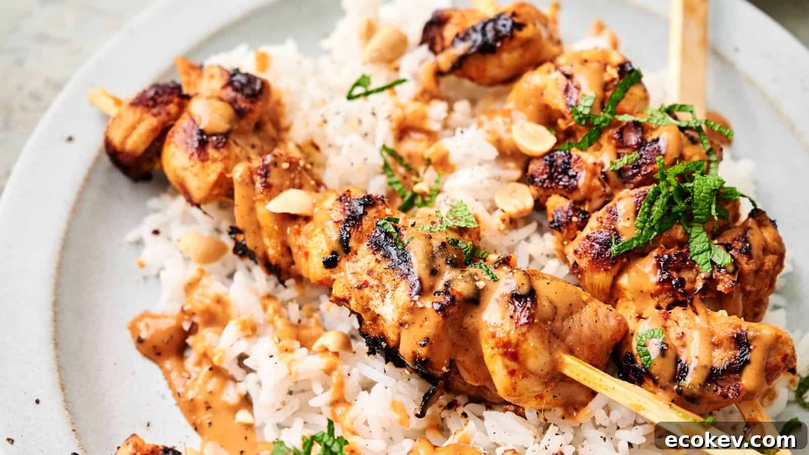 Thai chicken skewers topped with a creamy sauce and garnished with chopped herbs and peanuts, served over a bed of white rice.