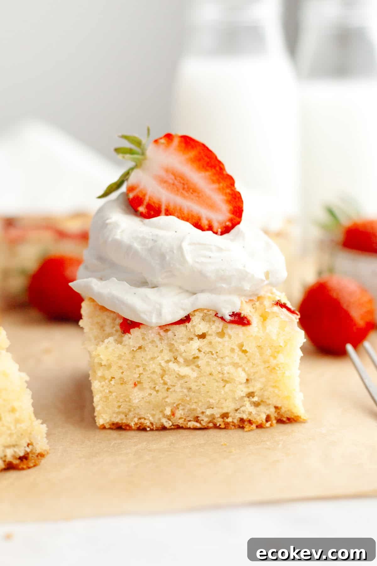 A close up of a slice of a mini strawberry cake, topped with whipped cream and half of a fresh strawberry.