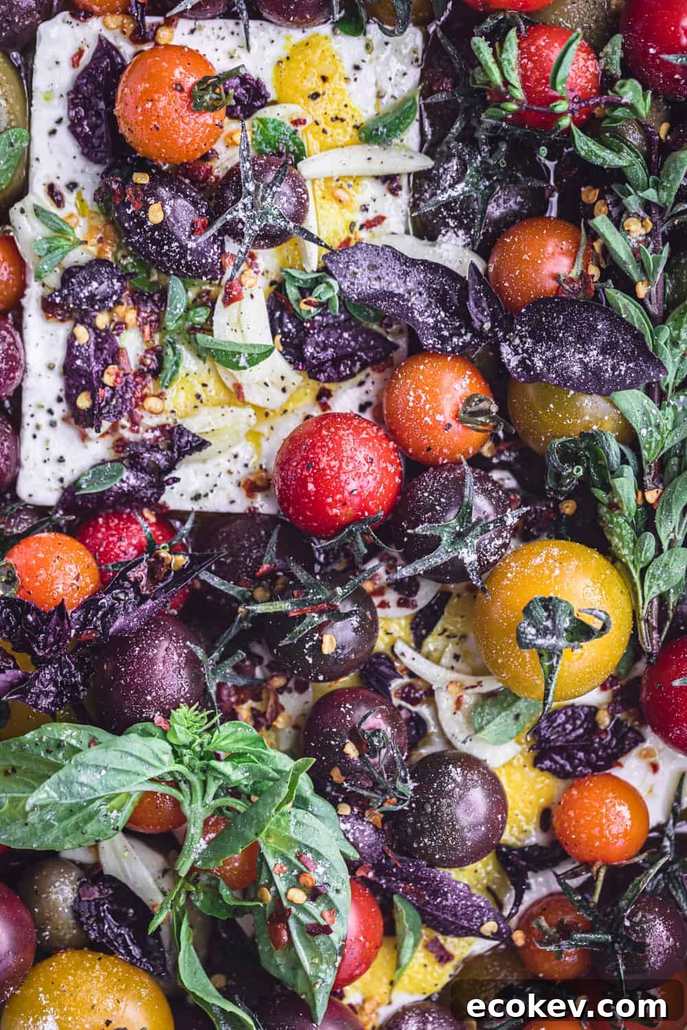Feta topped with colorful cherry tomatoes, garlic, lemon and fresh herbs; overhead shot.
