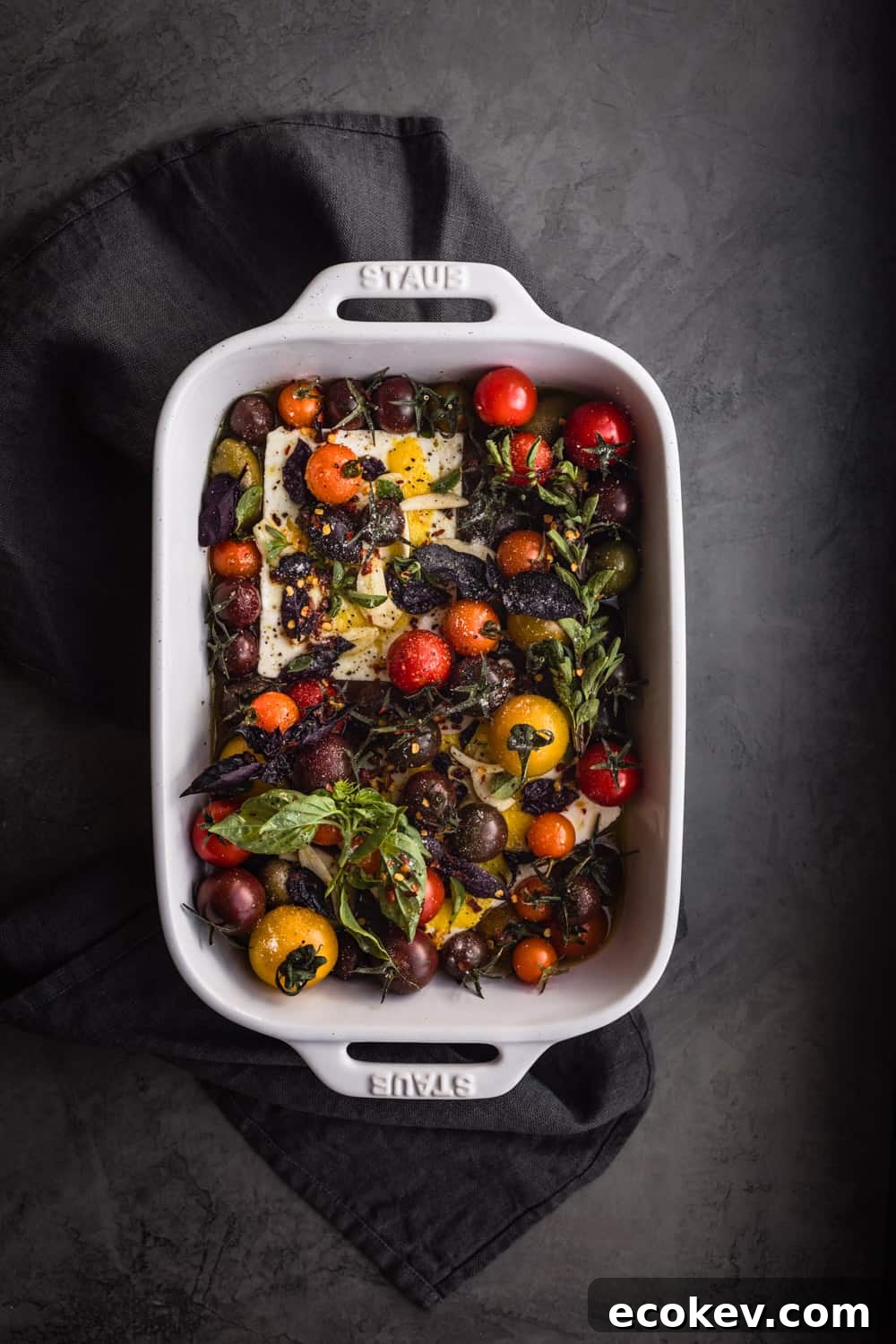 Feta with tomatoes, garlic, lemon, and fresh herbs in baking dish; overhead shot.