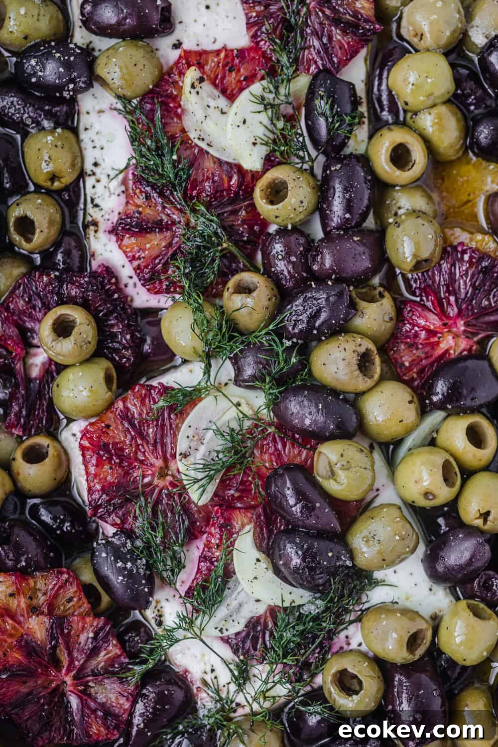 Baked feta dish - winter version topped with olives, blood orange and dill; overhead shot.