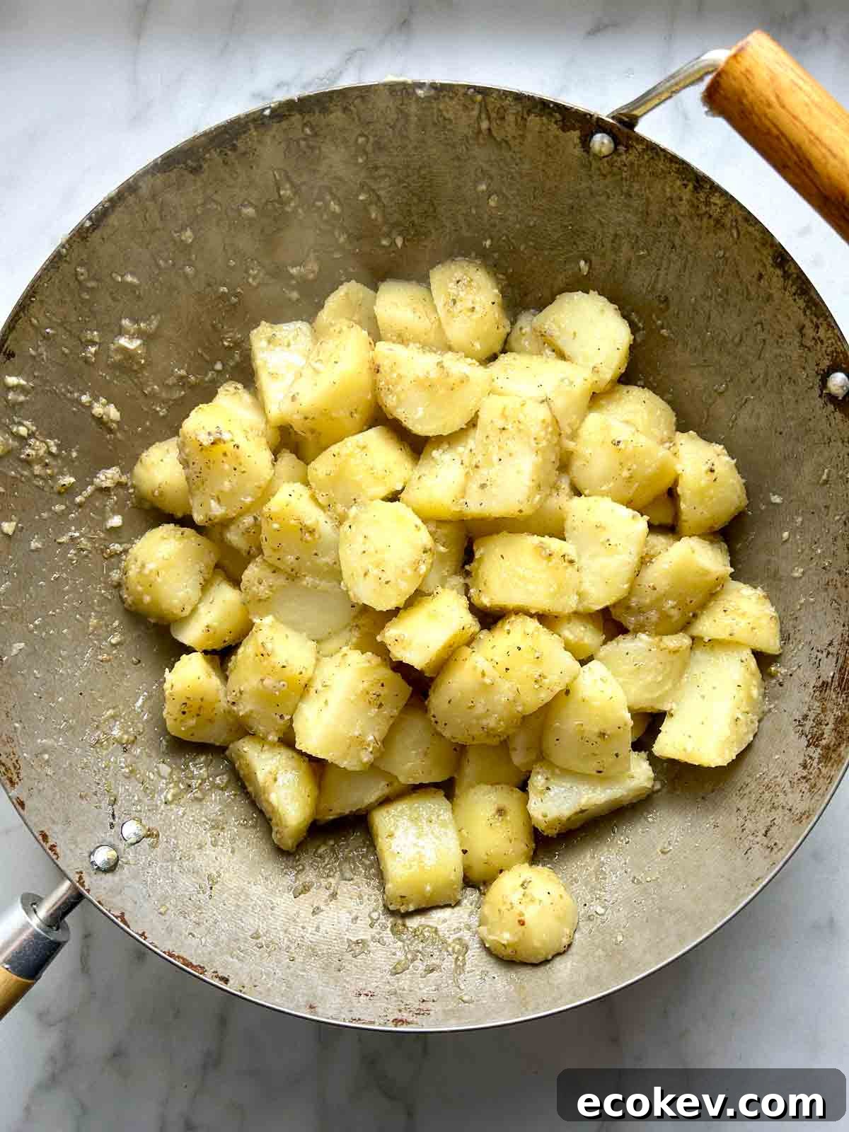 potato chunks being tossed with oil and seasonings in large wok.