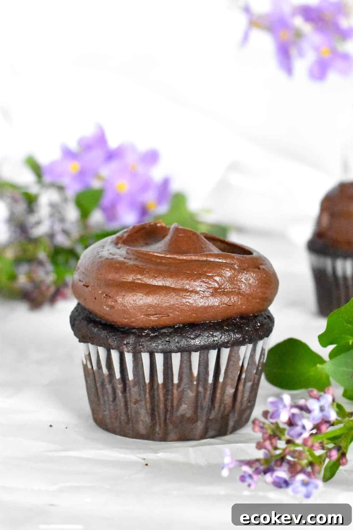chocolate cupcake with purple flowers in background. 