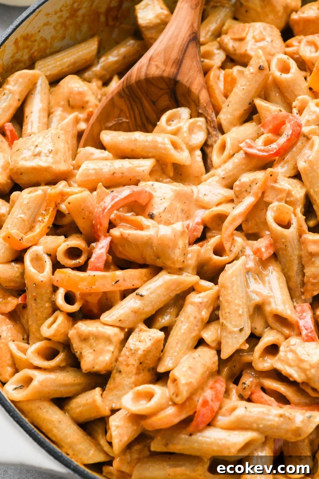 Close up shot of a spoon scooping creamy cajun chicken pasta out of a large ceramic skillet.
