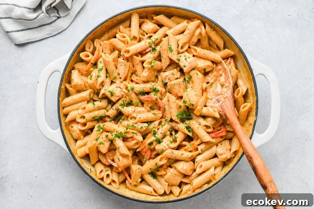 Large white ceramic skillet filled with creamy cajun chicken pasta, on a light colored background with a folded striped linen.