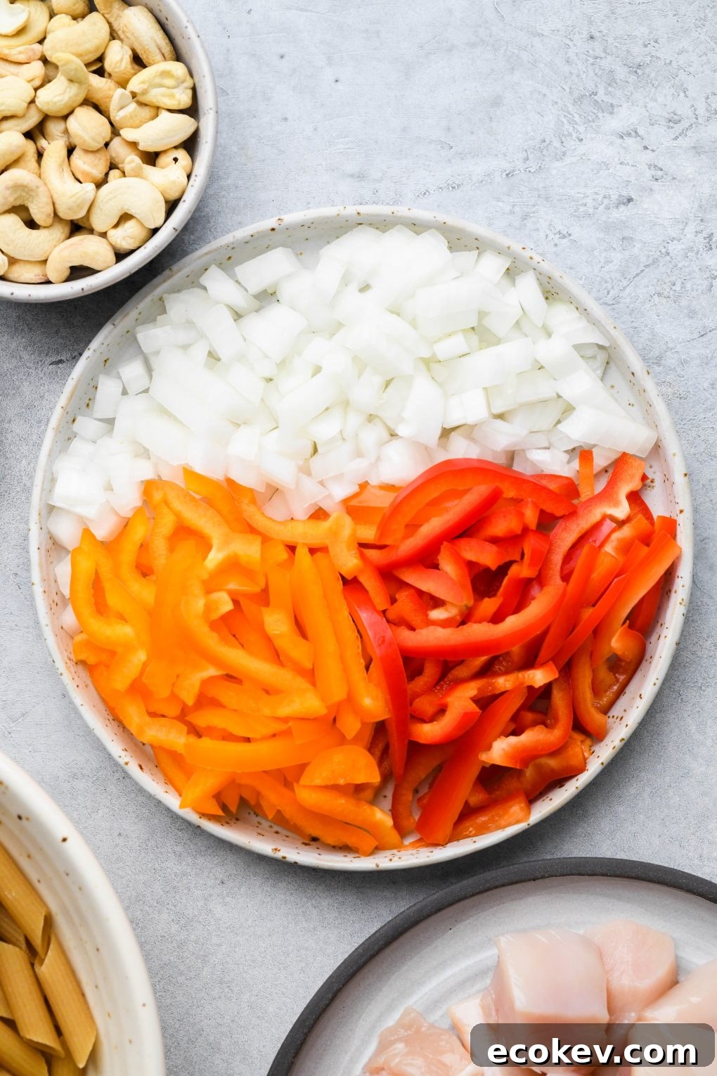 A large speckled white plate filled with chopped onion, orange pepper and red pepper on a light colored background.