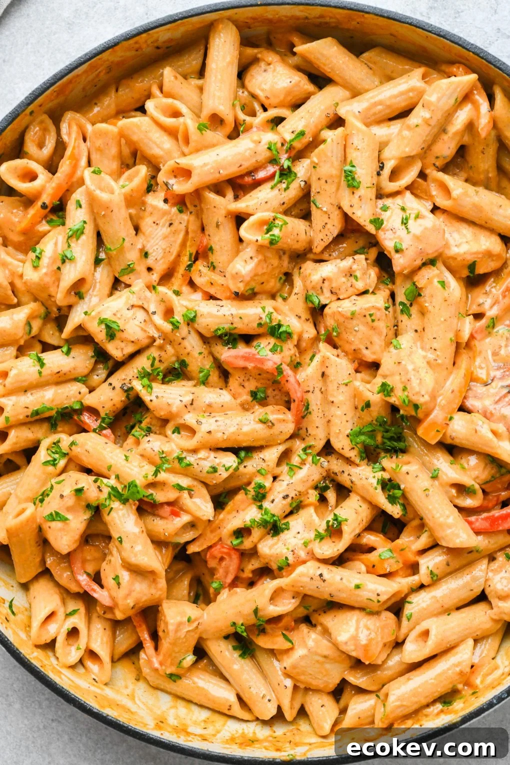 Close up image of a ceramic skillet filled with super creamy cajun chicken pasta. Topped with chopped parsley on a light colored background.