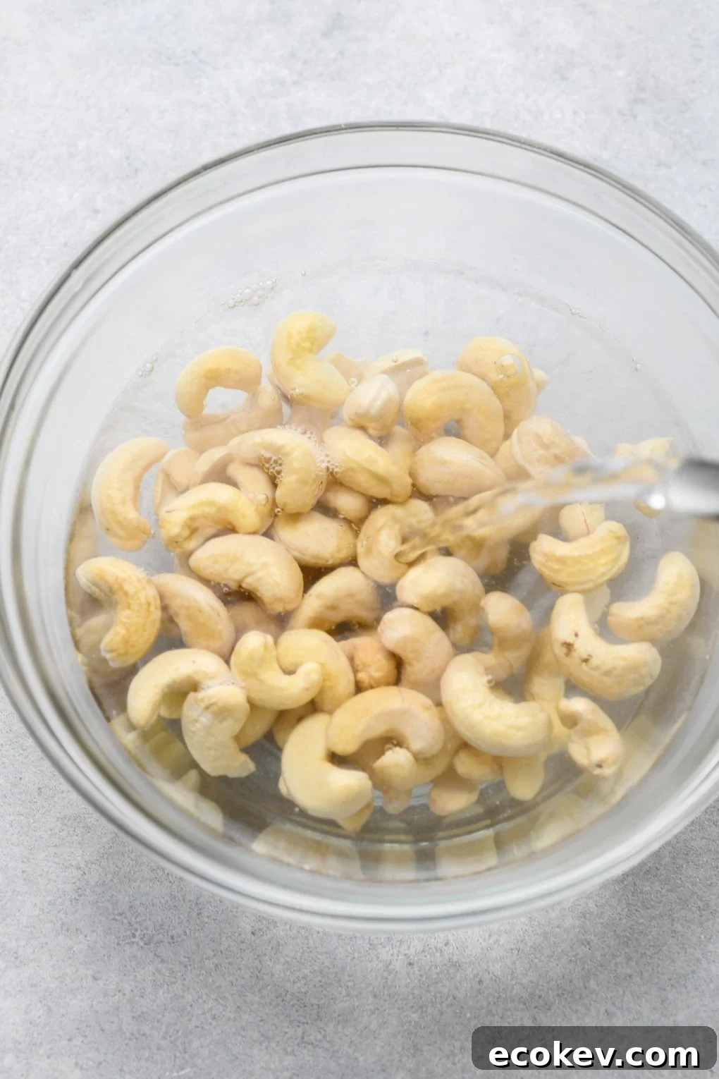 Raw cashews in a glass bowl being filled with hot water.
