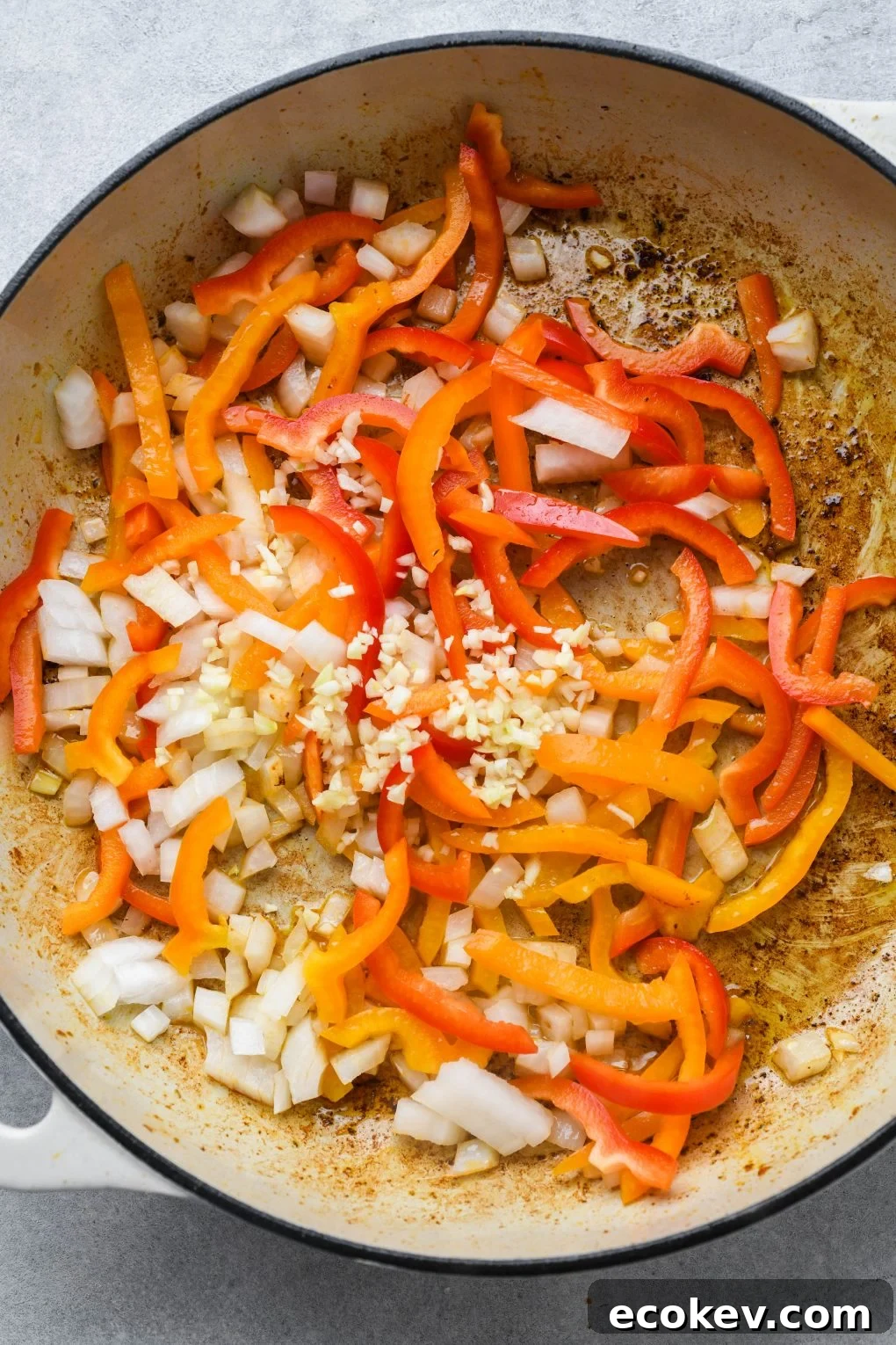 Chopped bell peppers, onion, and garlic, in a large white ceramic skillet. 