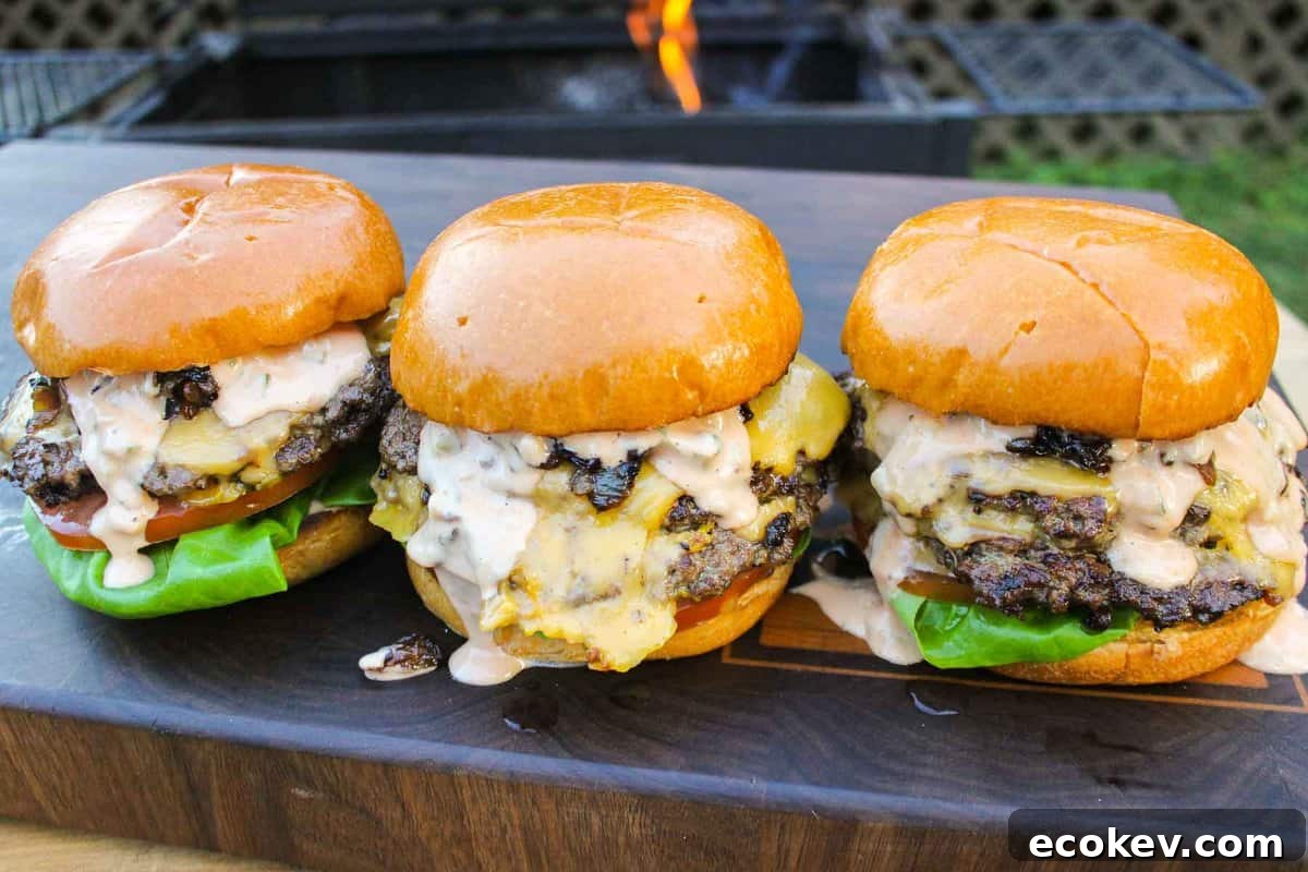 Three of the animal style burgers sitting on a cutting board together.