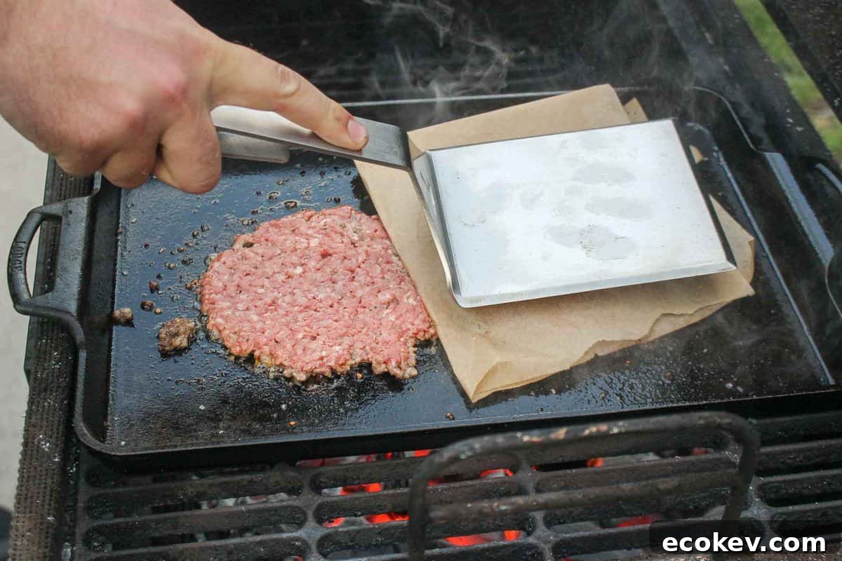 Smashing the burger patties on the skillet.