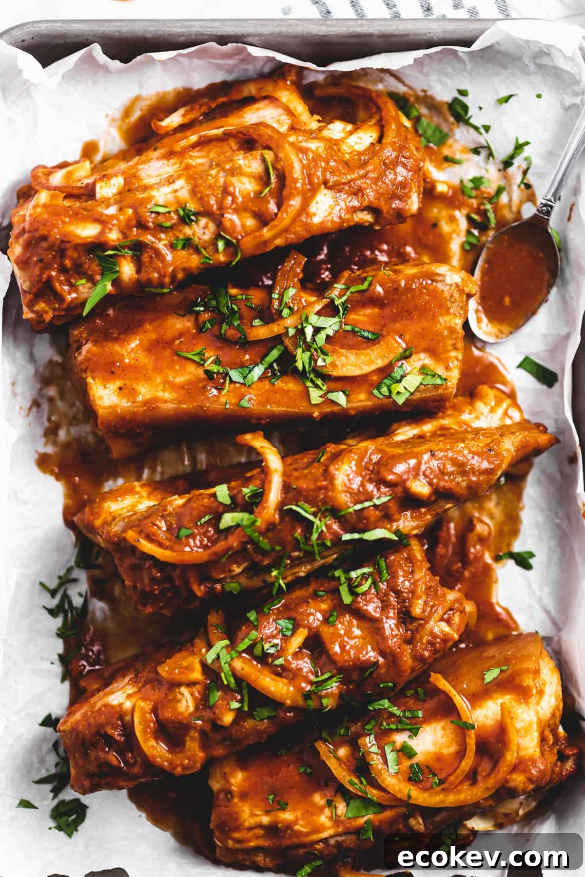 overhead photo of saucy country-style pork ribs in a baking dish, topped with onions and cilantro.
