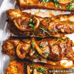 serving plate holding four country style pork ribs with onions and cilantro on top.