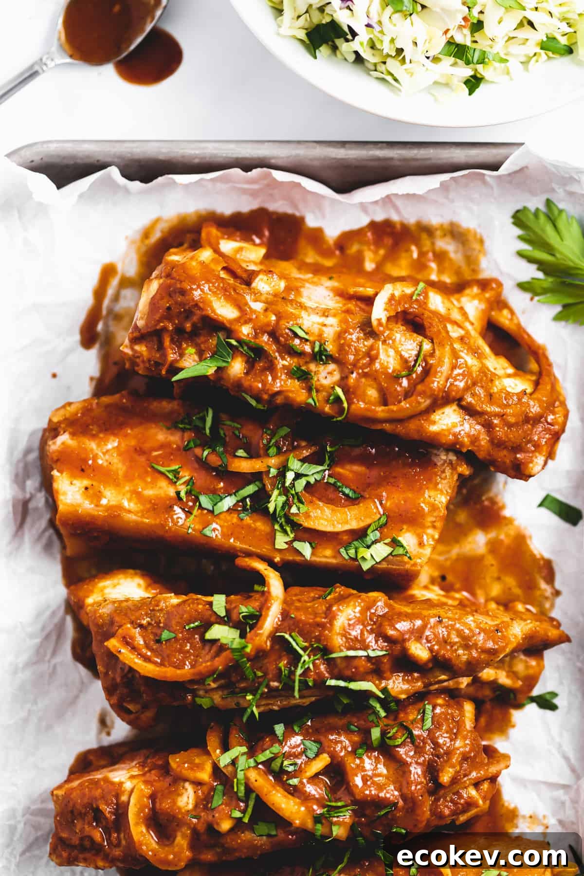 overhead photo of saucy country-style pork ribs in a baking dish, topped with onions and cilantro.