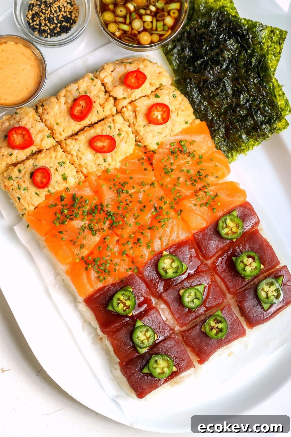 Nigiri-style sushi board with rice on the bottom and three different toppings, spicy crab, salmon and bluefin tuna. On a platter with different sauces on the side.