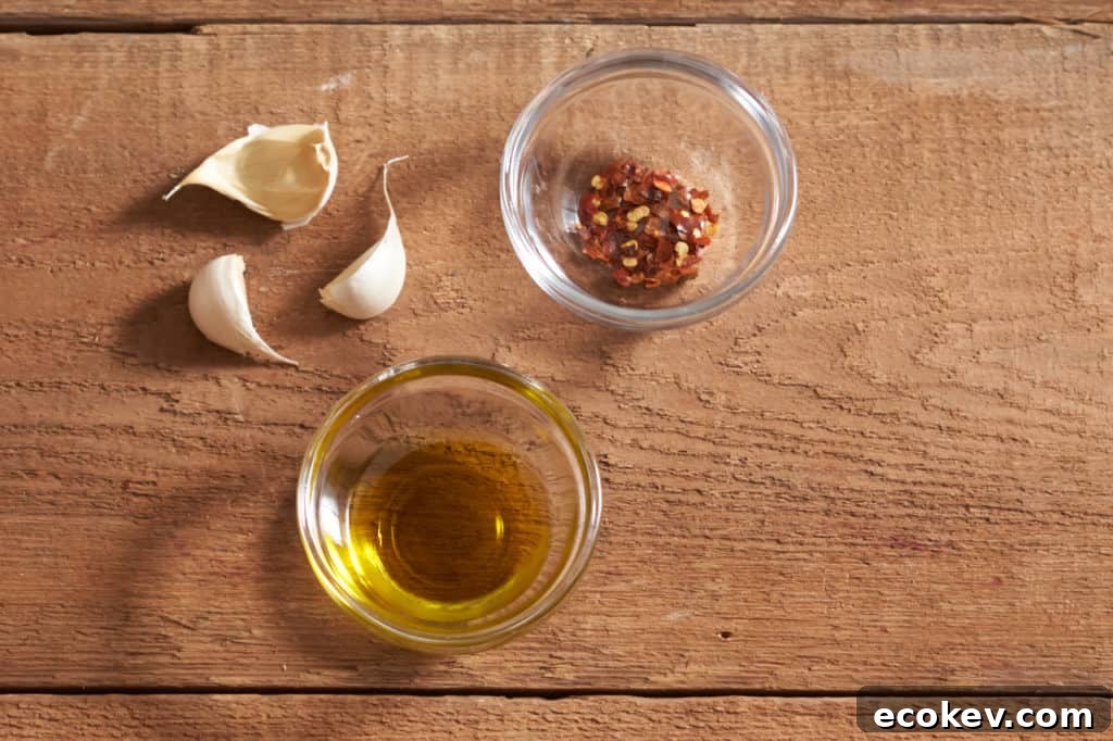 Three cloves of garlic and two small glass bowls with olive oil and crushed red pepper.