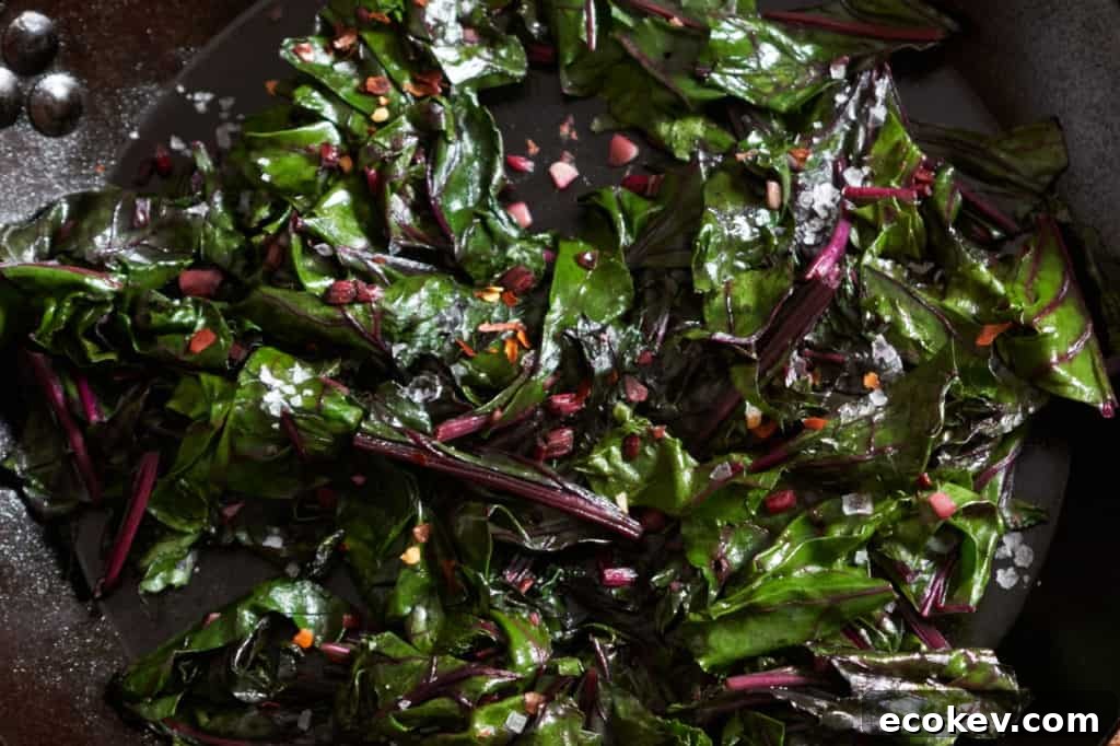 Finished sautéed beet greens in a cast iron skillet with bits of garlic and crushed red pepper on top.