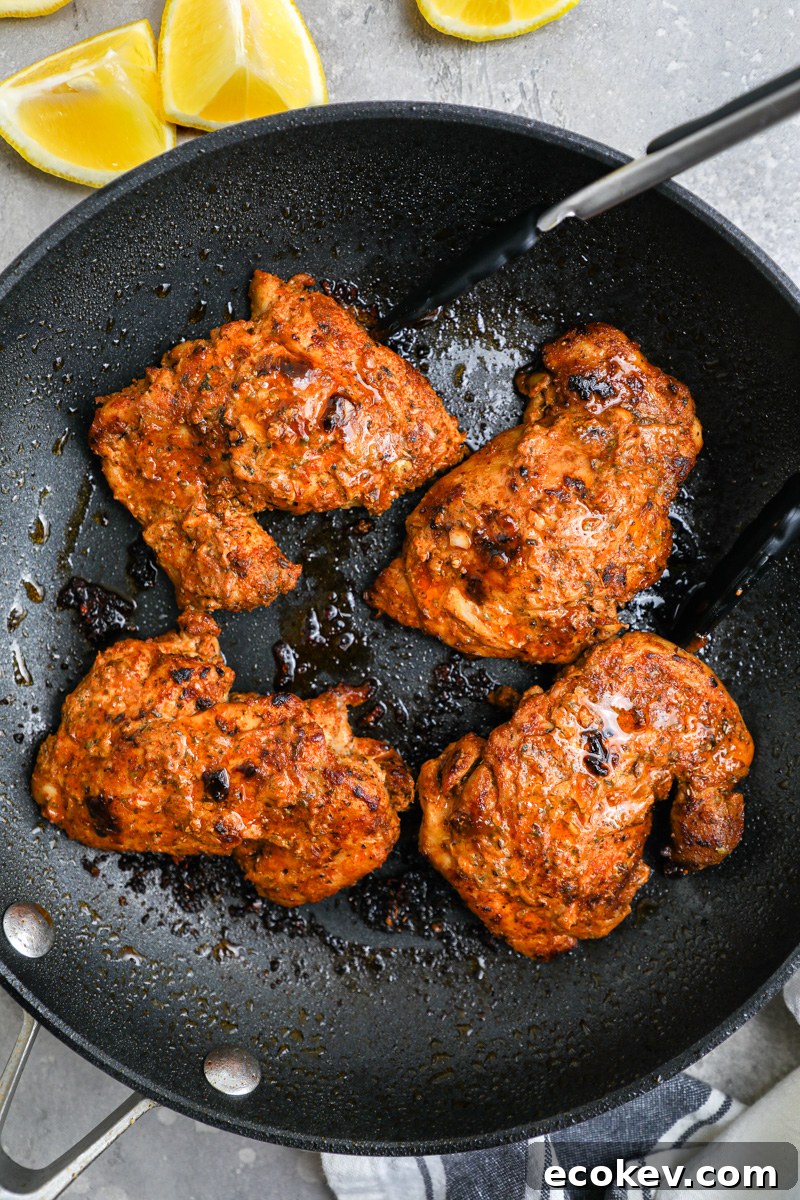 A large skillet filled with marinated chicken thighs sitting next to lemon wedges