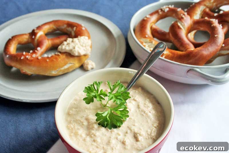 A bowl of German Bavarian Obatzda cheese dip in the center front and two plates with large lye pretzels in the rear. On a blue tablecloth.