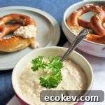 A bowl of German Bavarian Obatzda cheese dip in the center front and two plates with large lye pretzels in the rear. On a blue tablecloth.